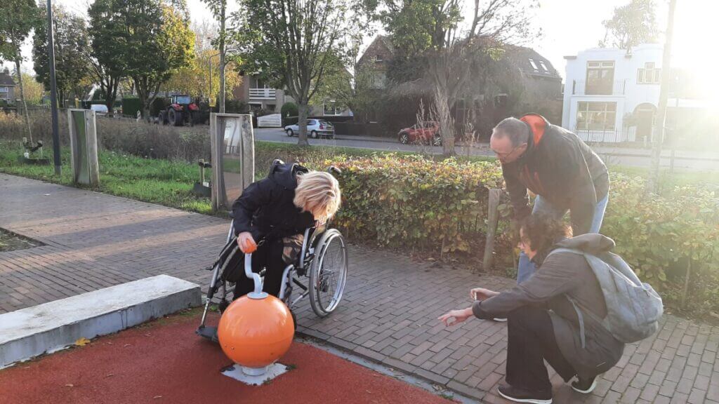 Playground. Person in wheelchair plays with a music ball. Two people comment on the action.